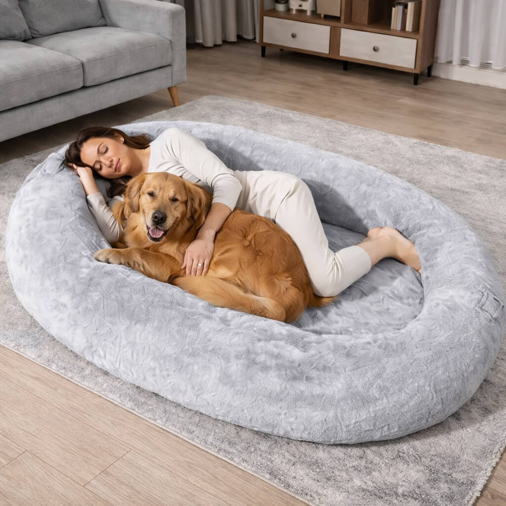 Woman and dog lying on a large gray dog bed in a living room.