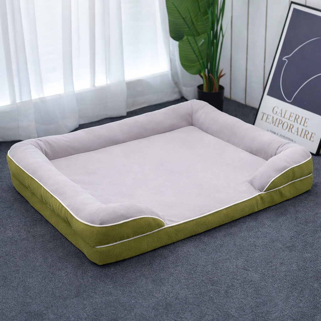Green and white Orthopedic Dog Bed on a gray floor with a plant and framed picture in the background.