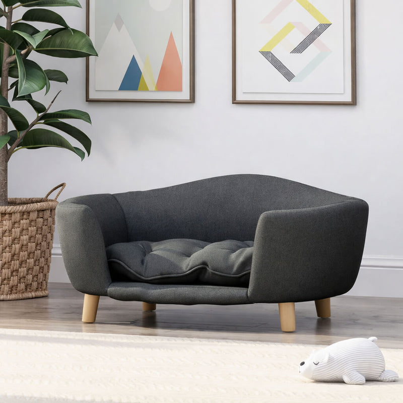 Gray  Luxury Dog Bed with wooden legs in a room with a plant and framed art on the wall.